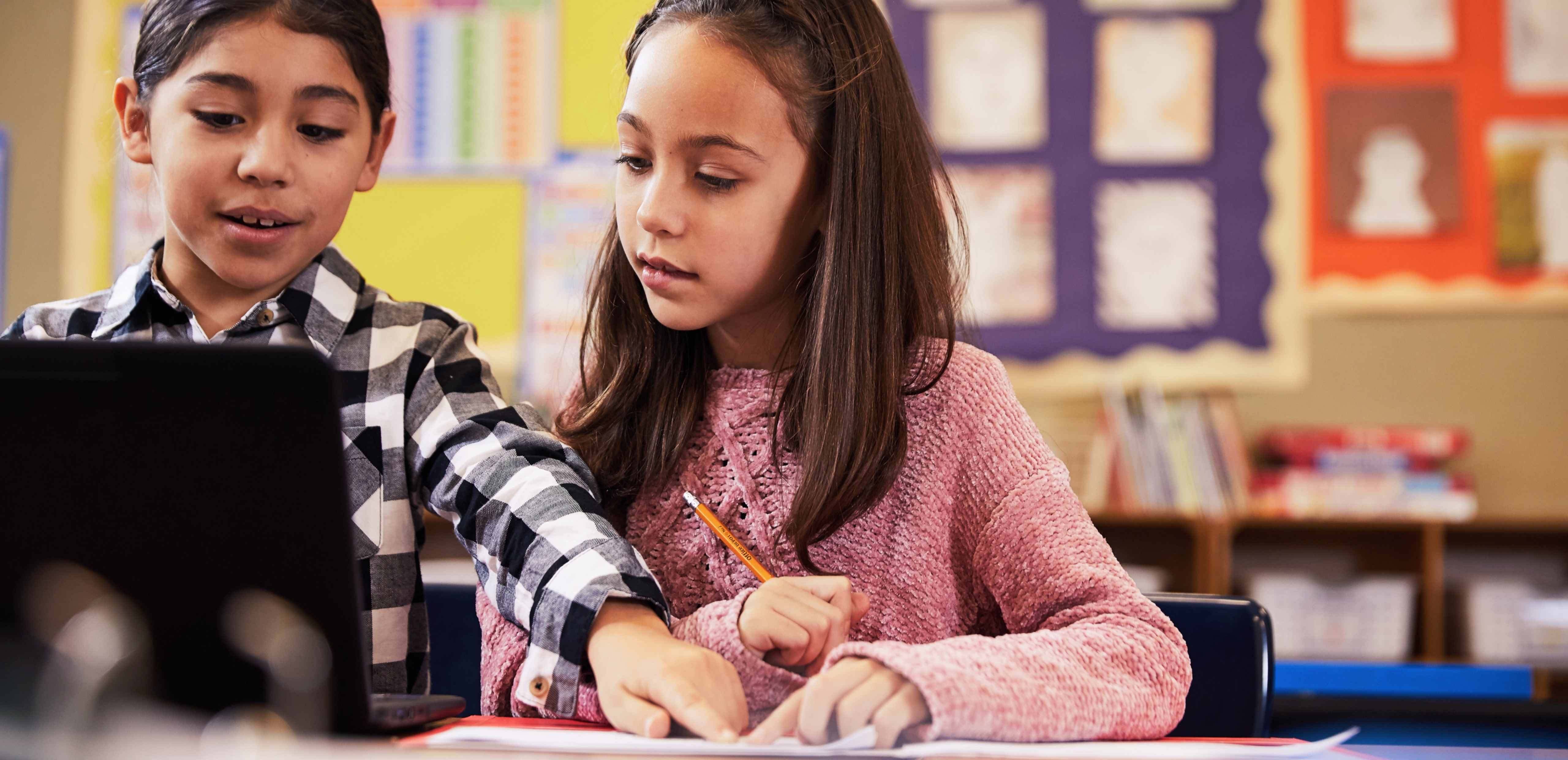Two students sitting at a desk collaborating in a classroom.