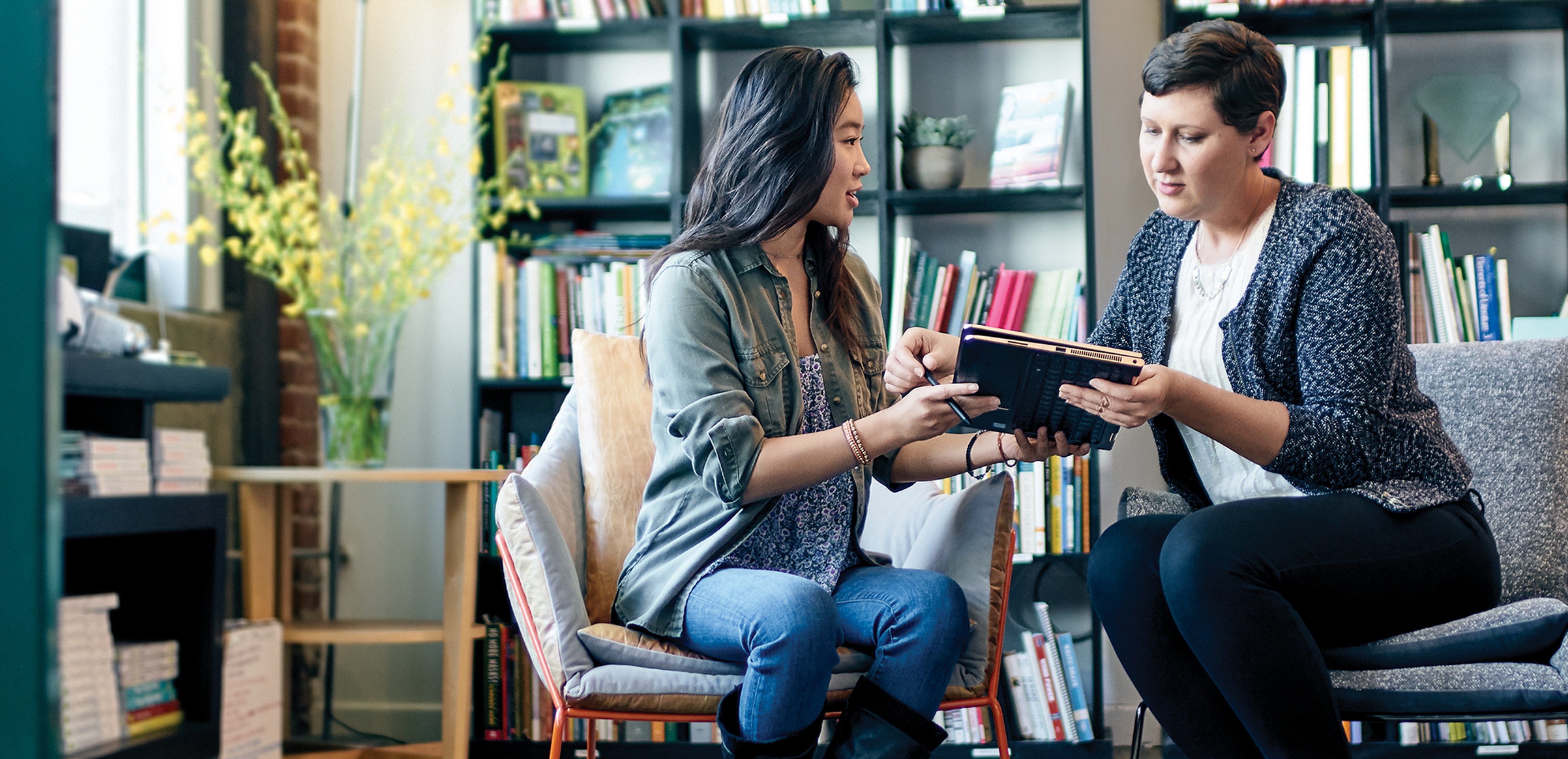 Two women sitting in chairs holding a Windows 10 tablet.