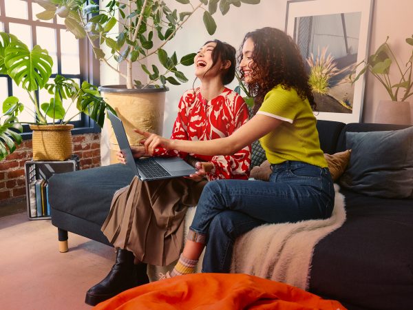 Two women sitting on a couch enjoying what they're watching on a laptop computer