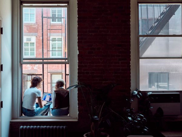 Two people talking while sitting in an open window in a city