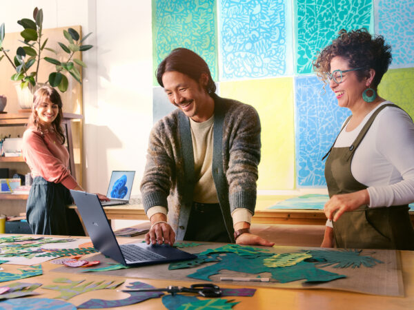 Three people smiling as they work on laptop computers in a creative studio.