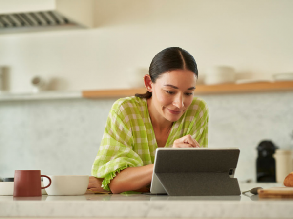Woman smiles as she enters something into her tablet device in her kitchen